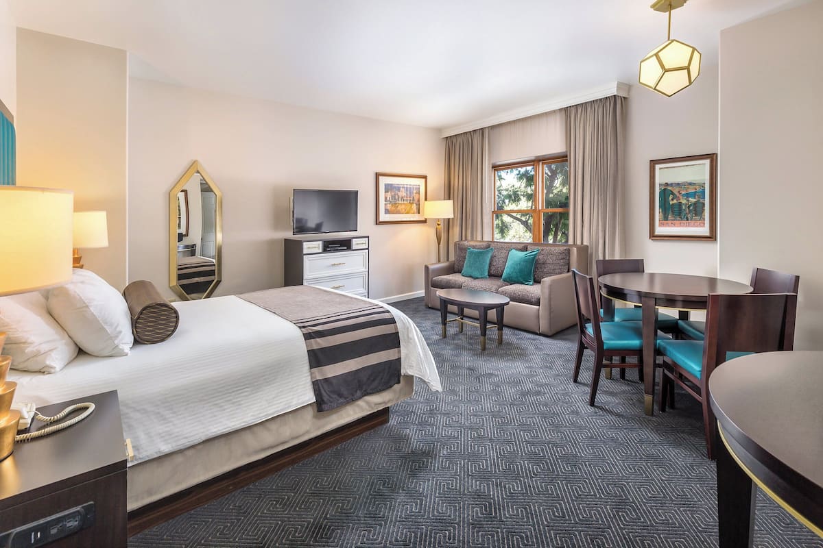A hotel room with a bed, a TV, a sofa, a dining table, and chairs.