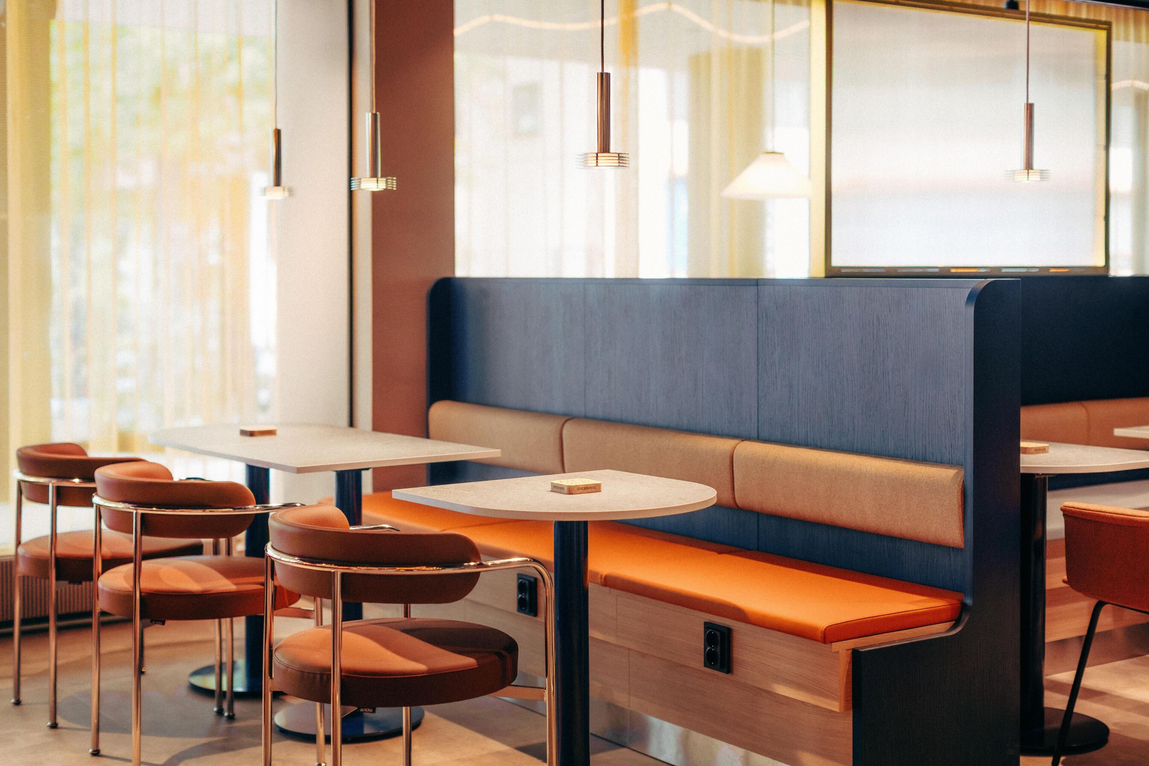 Een modern restaurant met zitplaatsen, ronde tafels en hanglampen.