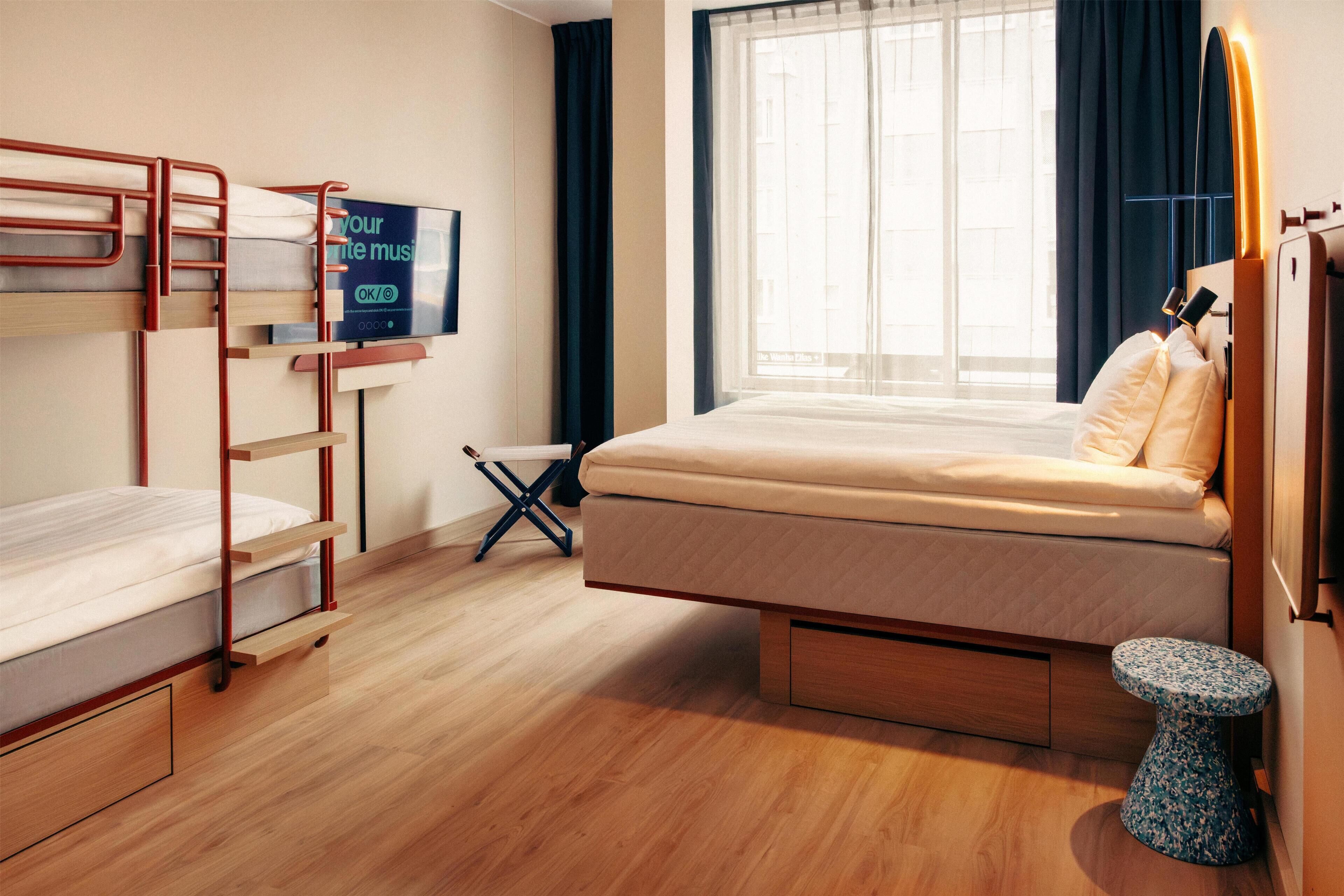 A room with a bunk bed, a single bed, a TV, a window with curtains, and a small round table.