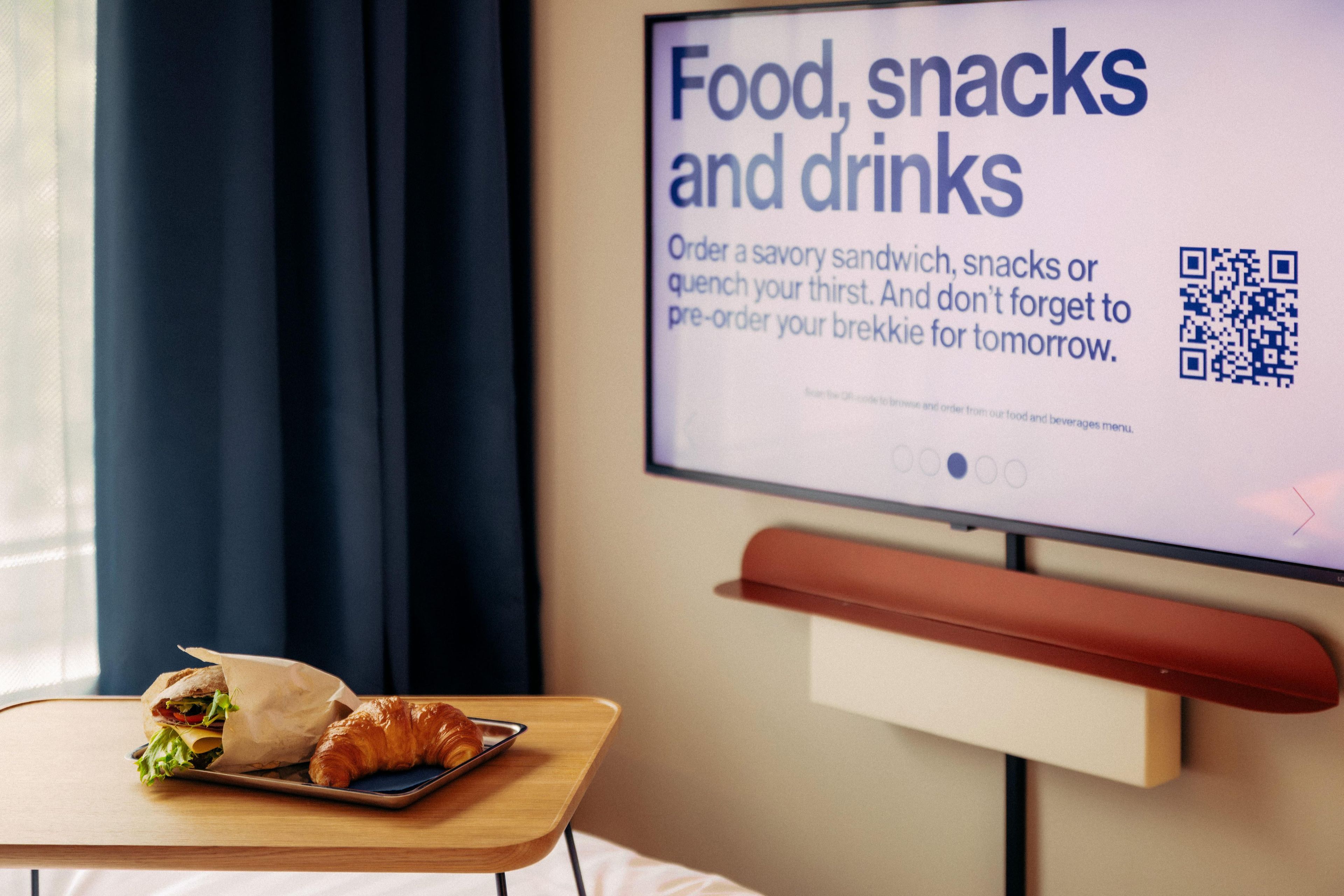 A hotel room with a television screen displaying a menu for food, snacks, and drinks.