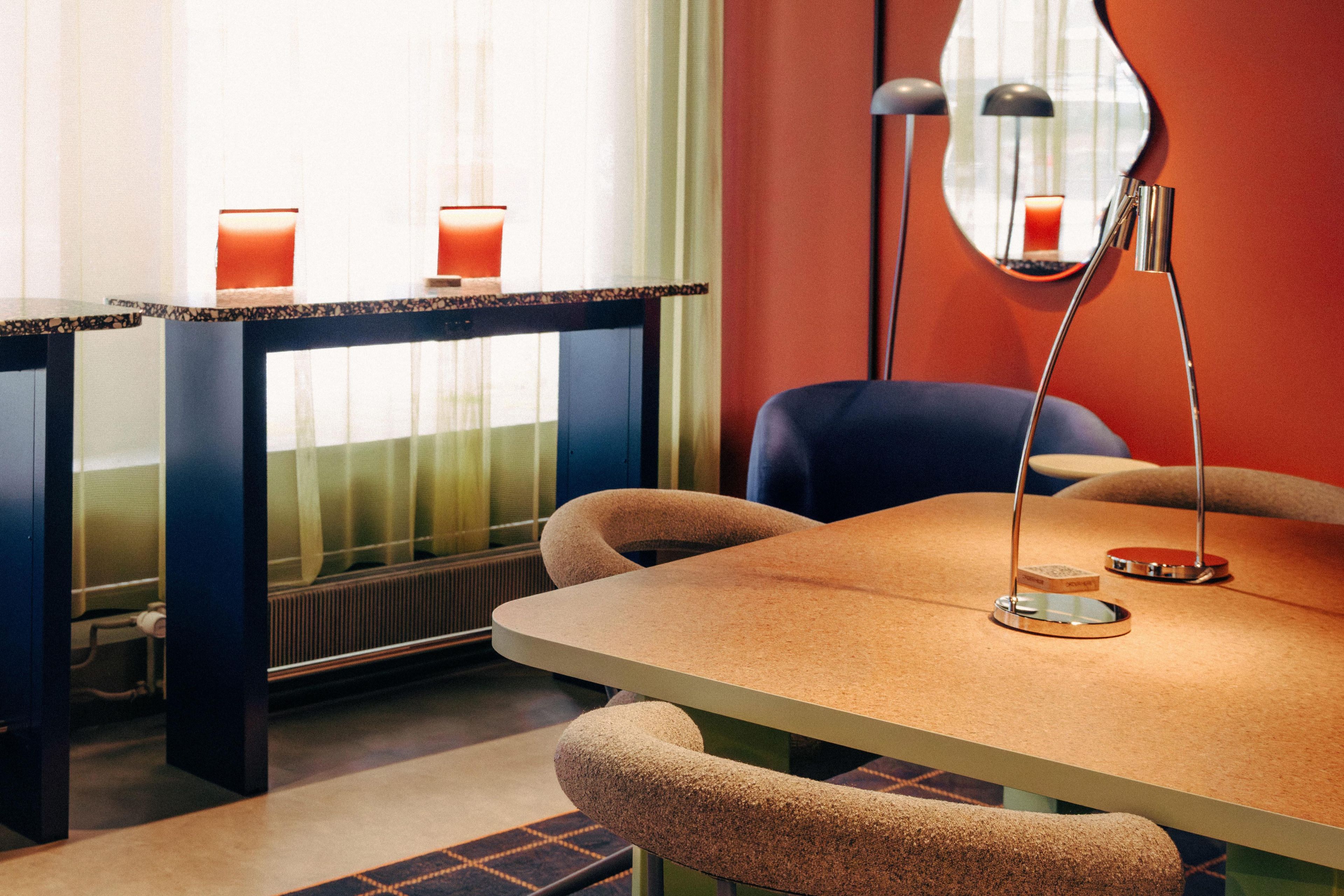 A modern room with a round table, two chairs, a side table, a mirror, and two candles on the table.