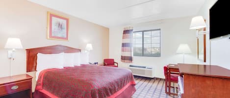 A hotel room with a large bed, two bedside tables, a desk, a chair, a window with curtains, and a wall-mounted TV.