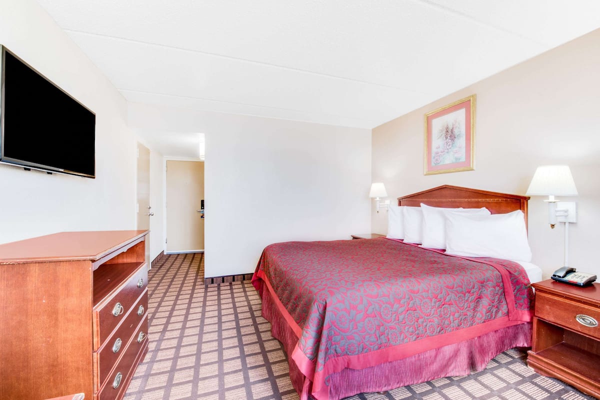 A hotel room with a large bed, a dresser, a television, and a framed picture on the wall.