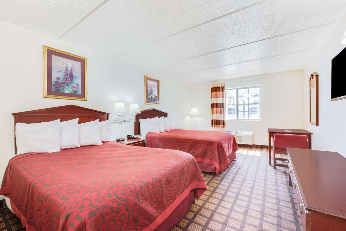 A hotel room with two beds, a desk, a chair, a TV, and a window with curtains.