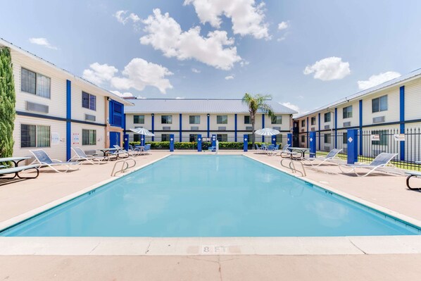 A swimming pool with lounge chairs and umbrellas, surrounded by a building with multiple floors and a blue and beige color scheme. - Days Inn & Suites by Wyndham Laredo (Laredo)