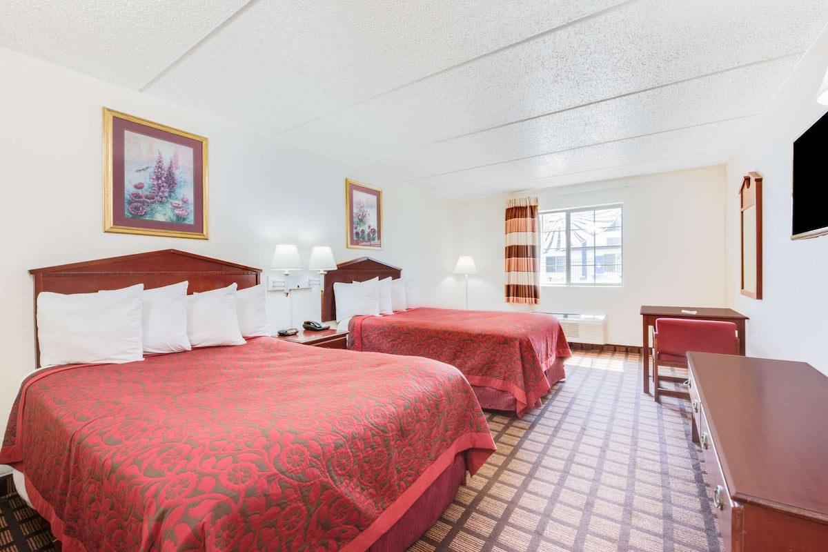 A hotel room with two beds, a desk, a chair, a TV, and a window with curtains.