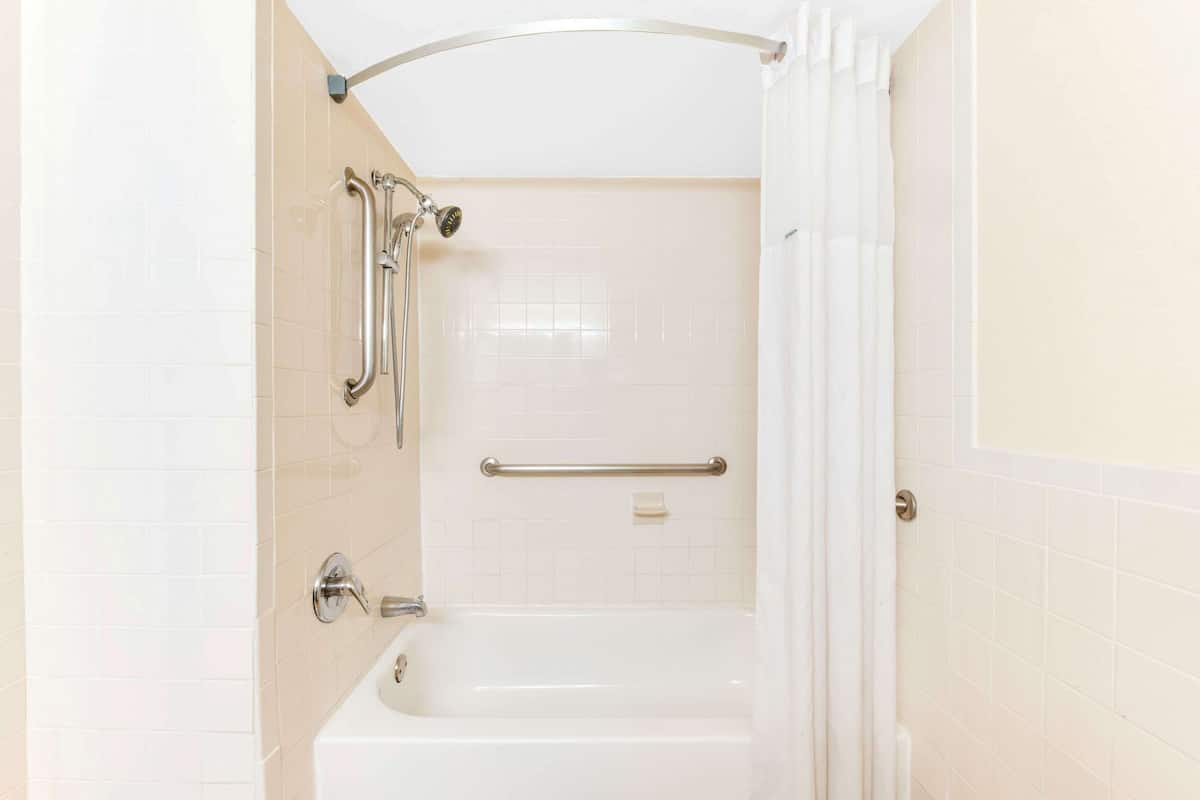 A bathroom with a bathtub, a shower with a grab bar, and a handrail.