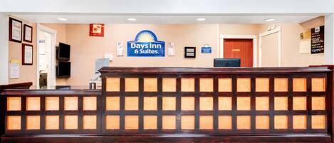 A reception desk with a Days Inn & Suites sign, framed certificates, and a closed door.