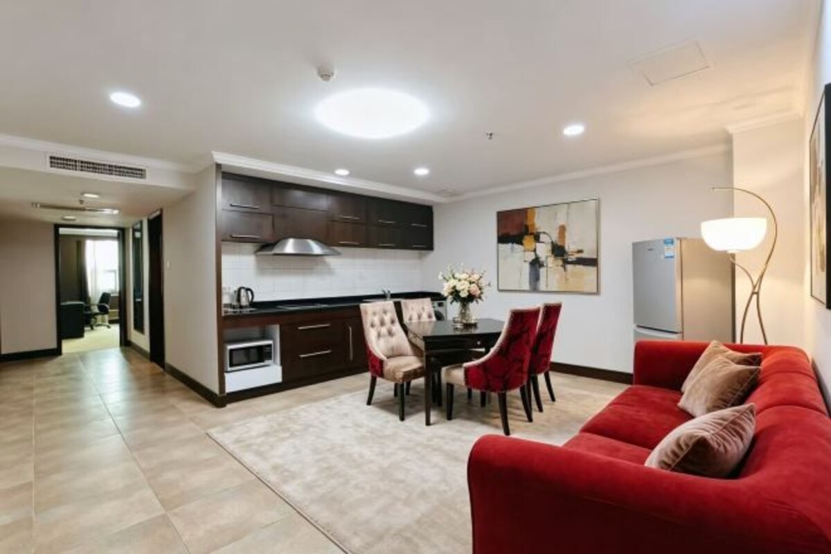 Una sala de estar moderna con un sofá rojo, una mesa de comedor con sillas, una zona de cocina y un espejo grande en la pared.