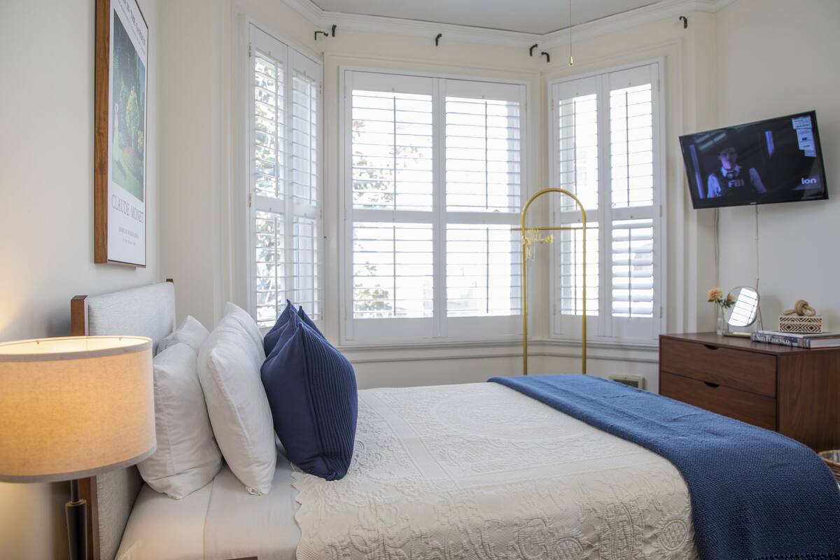 Quarto com cama, televisão e janela com persianas.