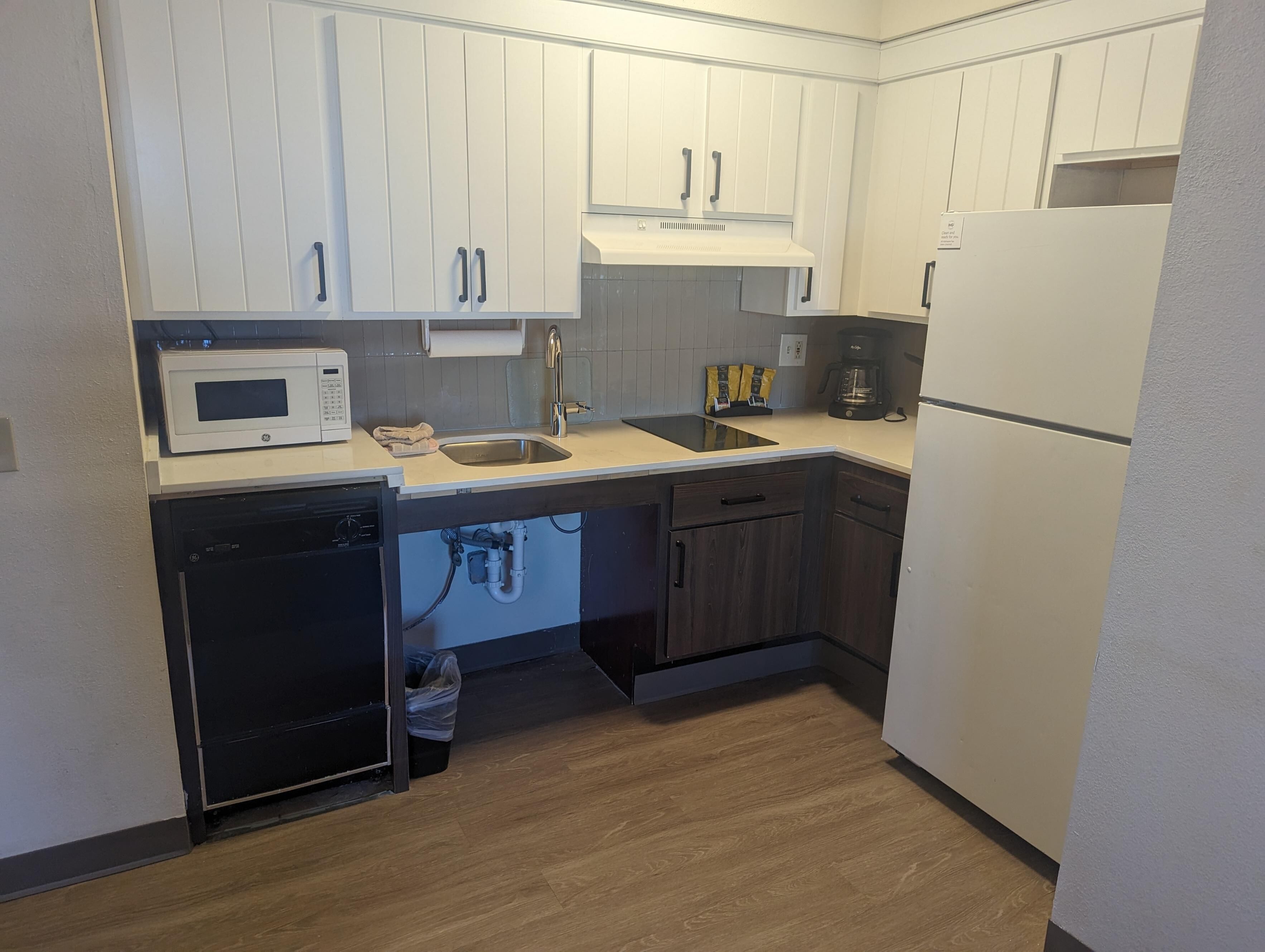A compact kitchen with white cabinets, a built-in microwave, a sink, and a dishwasher.