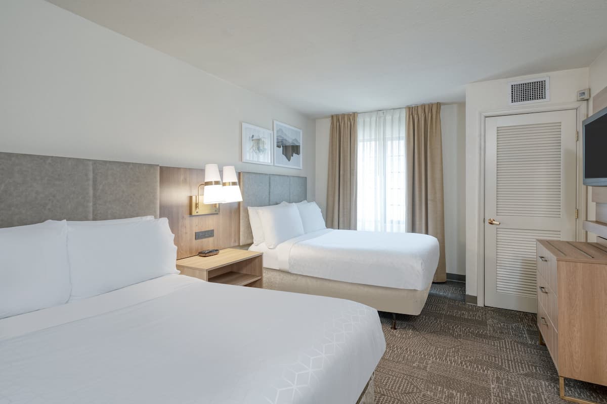 Une chambre d’hôtel avec deux lits, un bureau avec une lampe, une télévision et une armoire.