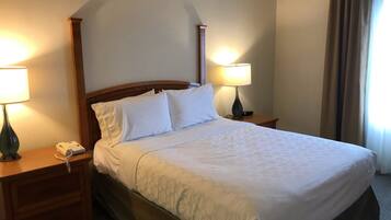 A neatly made bed with white linens, two bedside lamps, a wooden nightstand, and a telephone.