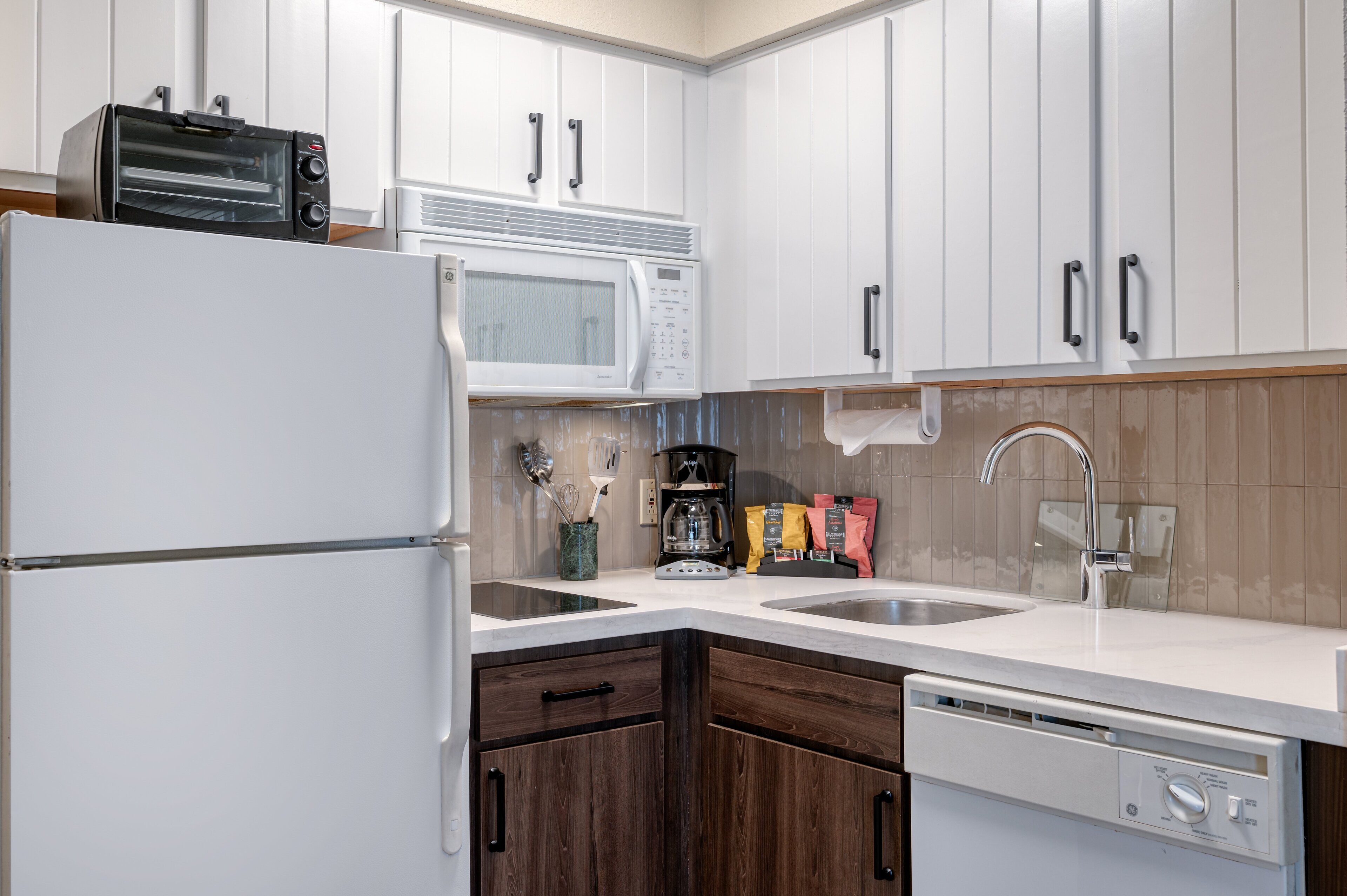 Una cocina con gabinetes blancos, microondas, cafetera y lavavajillas.