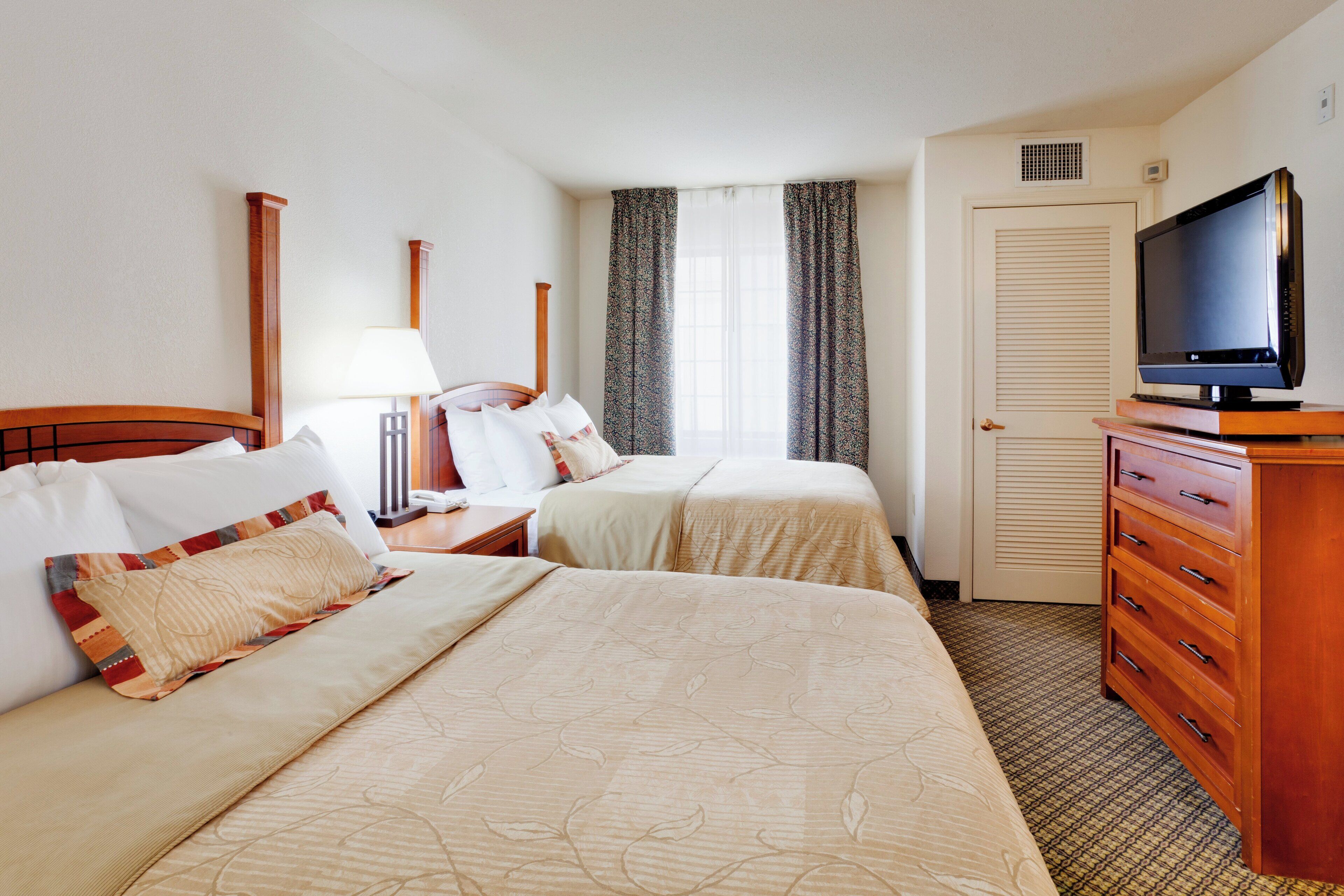 Quarto de hotel com duas camas, televisão, cômoda e janela com cortinas.