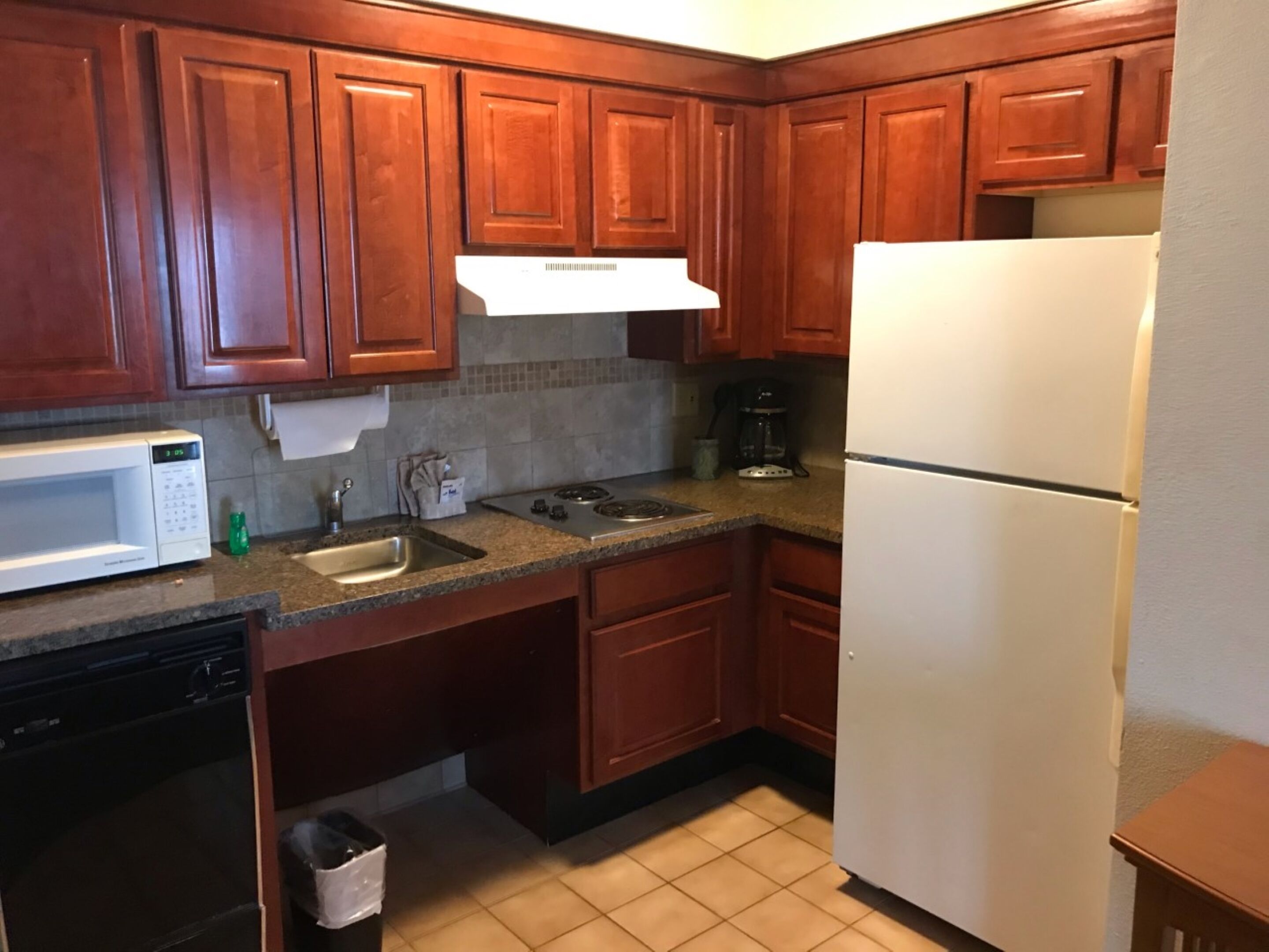 A kitchen with wooden cabinets, a white microwave, a sink, a stove, and a refrigerator.