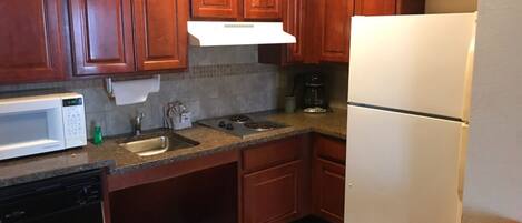 A kitchen with wooden cabinets, a white microwave, a sink, a stove, and a refrigerator.