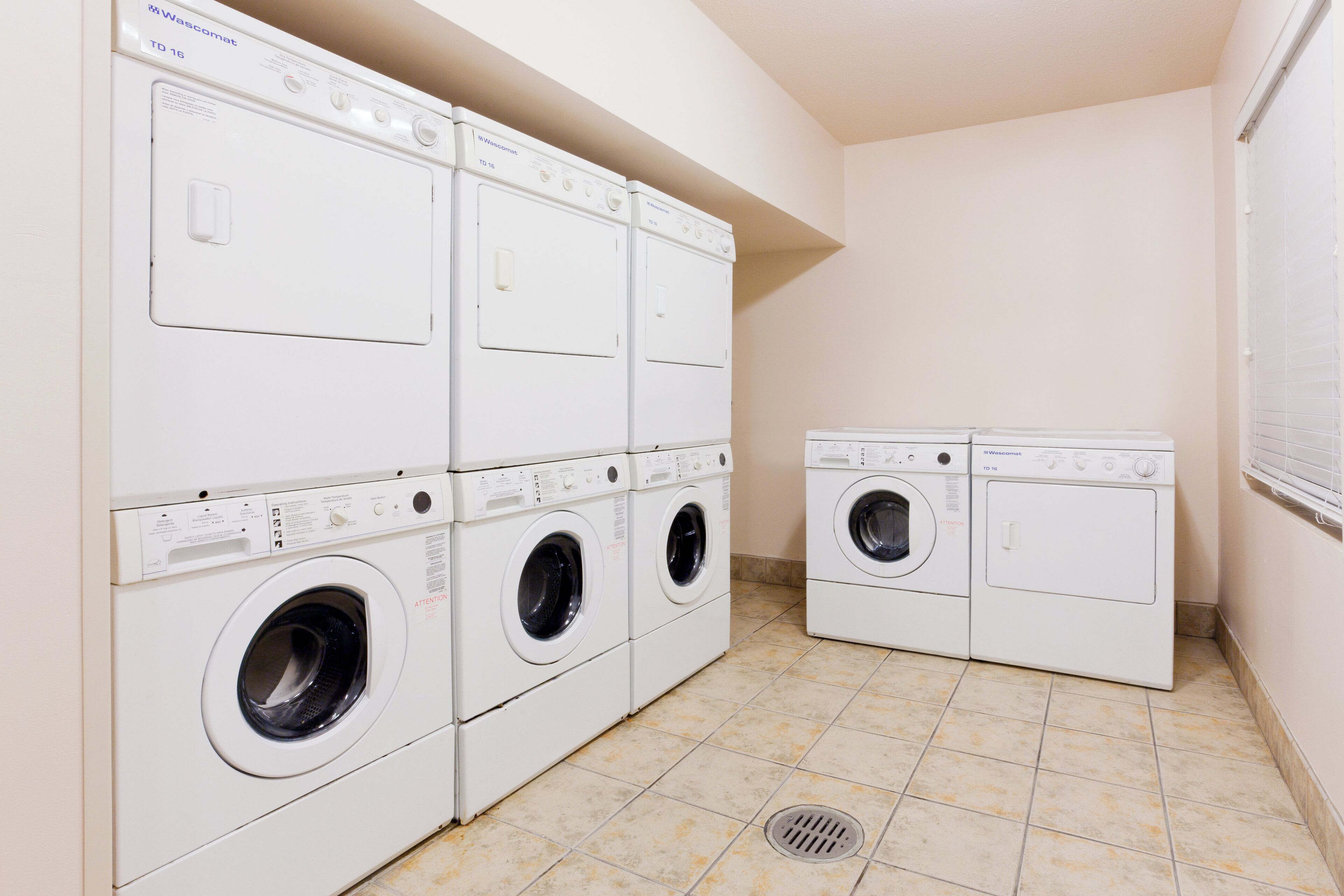 A laundry room with multiple Wascomat washing machines, a tiled floor, and a vented ceiling.