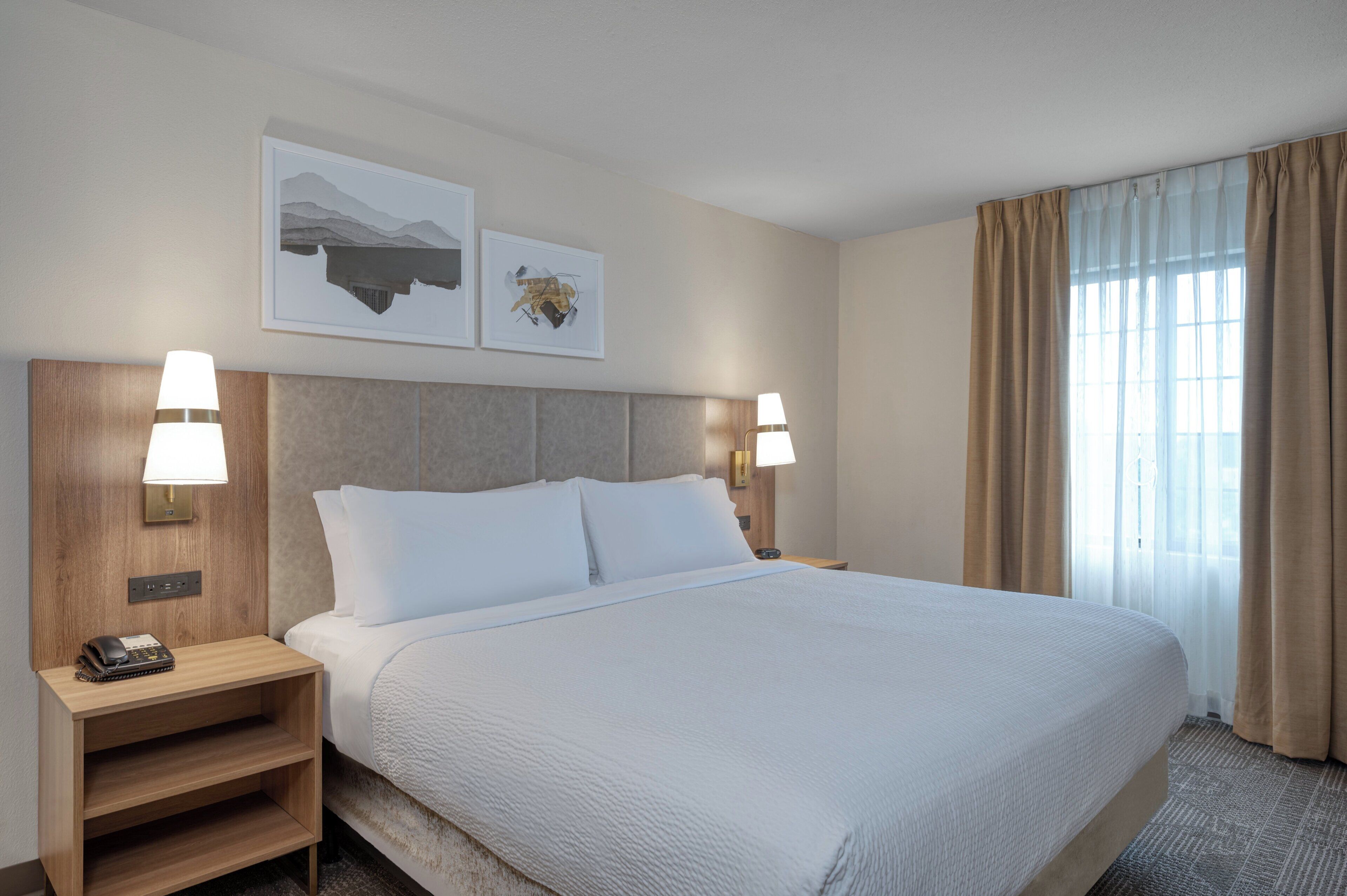 Una habitación de hotel con una cama grande, dos lámparas de noche, una mesita de noche y dos cuadros en la pared.