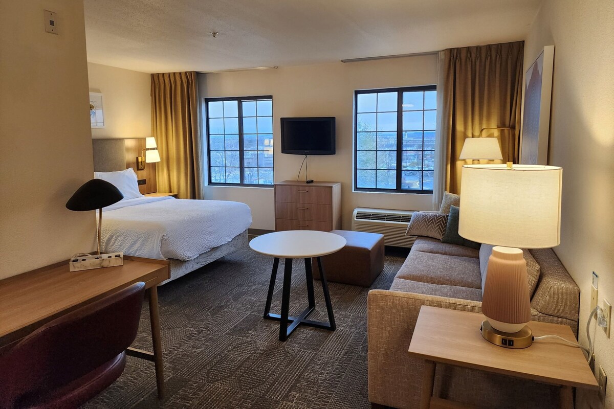 Ein Hotelzimmer mit einem Bett, einem Schreibtisch, einem Stuhl, einer Couch, einem Fernseher und einem Fenster mit Blick.