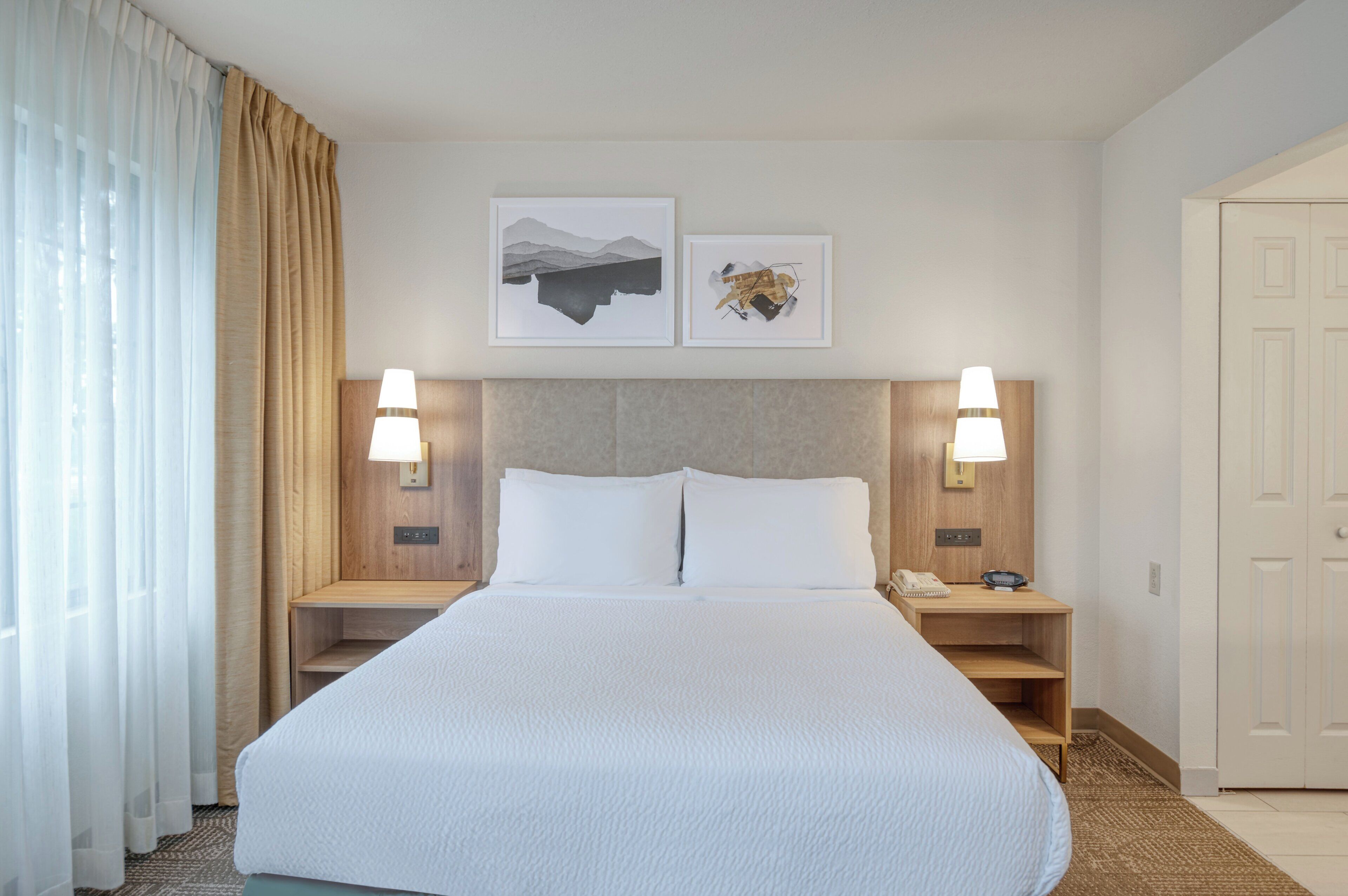 A hotel room with a large bed, two bedside tables with lamps, a wooden headboard, and two framed pictures on the wall.