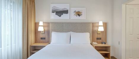 A hotel room with a large bed, two bedside tables with lamps, a wooden headboard, and two framed pictures on the wall.