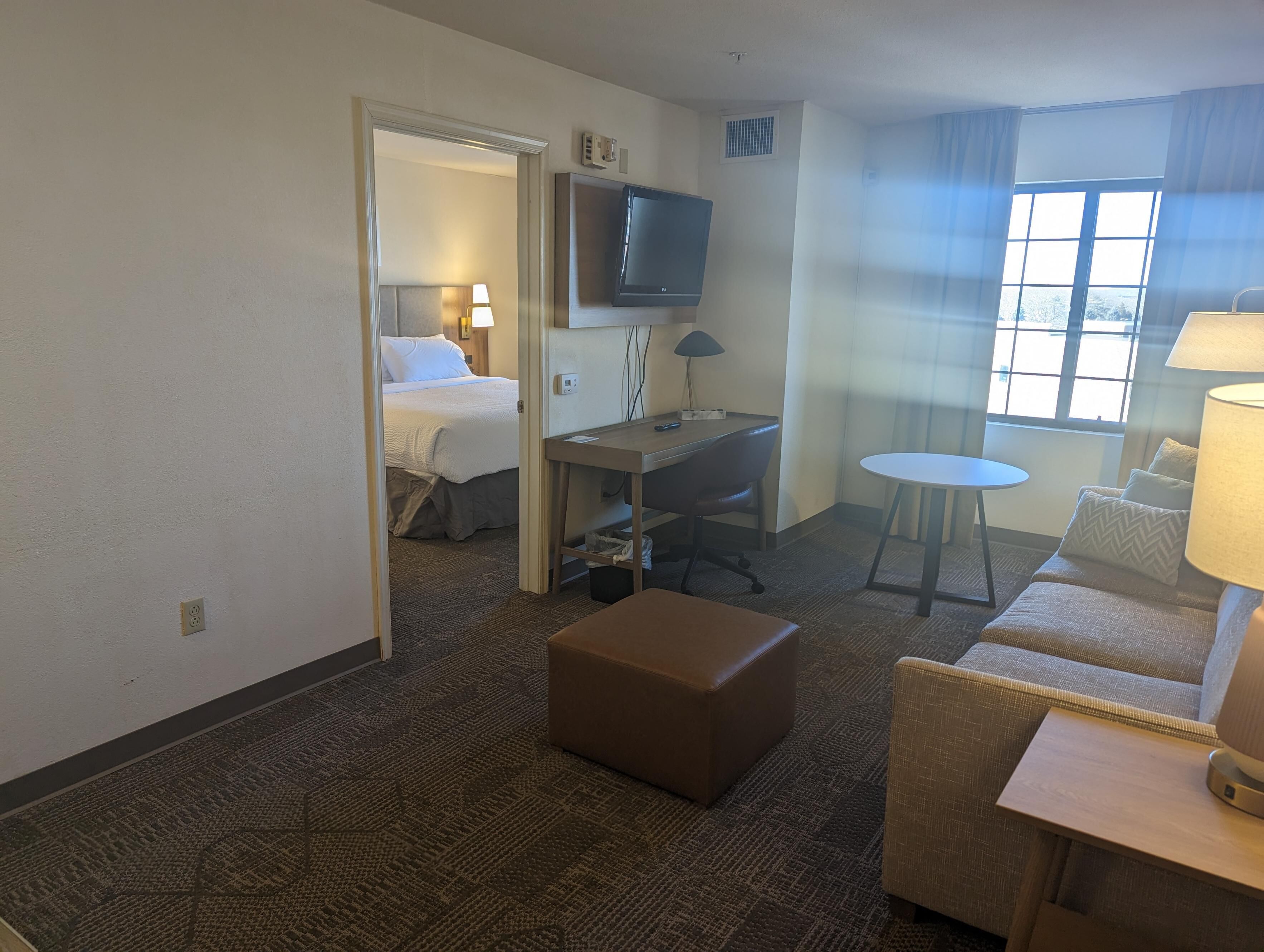 Habitación de hotel con cama, escritorio, silla, reposapiés y televisor.