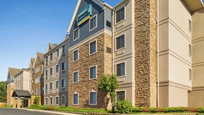 Un hôtel à plusieurs étages, doté d’une façade en pierre, d’une enseigne bien visible indiquant « Staybridge Suites », et d’un parterre aménagé devant l’entrée.