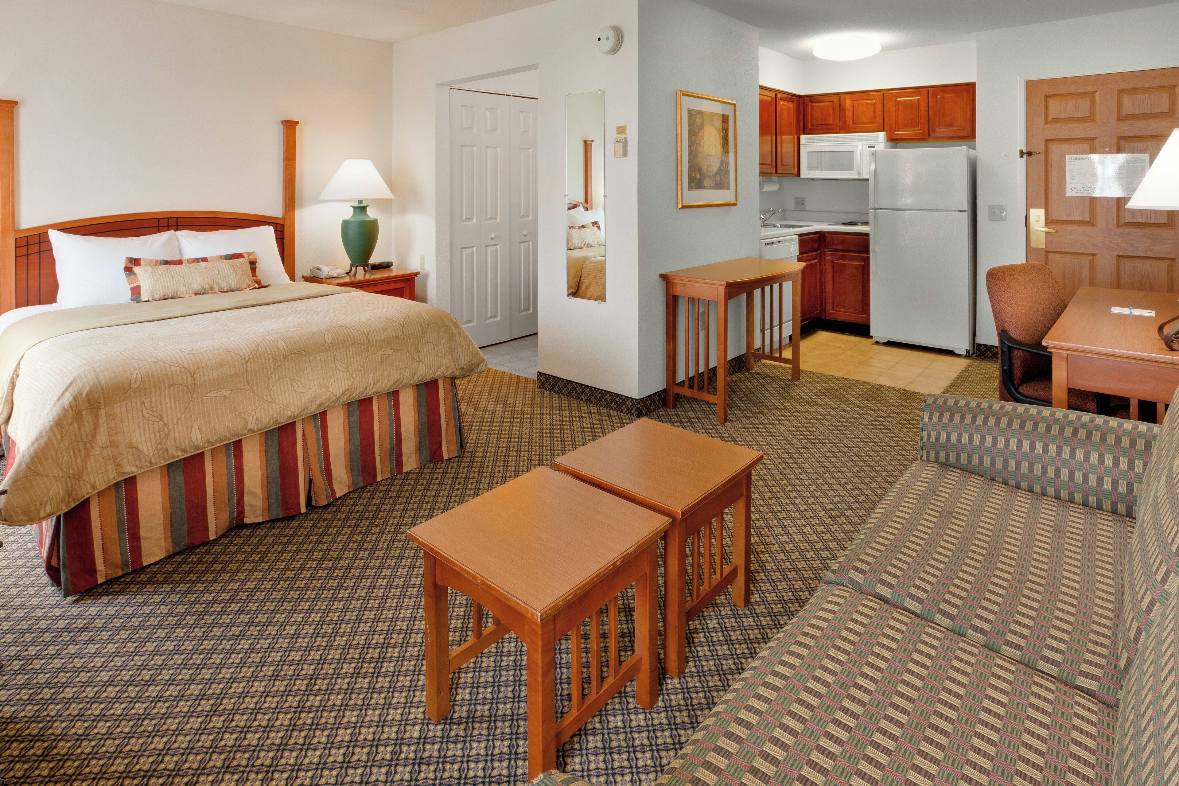 A hotel room with a bed, a desk, a chair, a sofa, a kitchenette, and a bathroom.