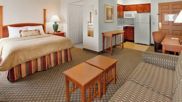 A hotel room with a bed, a desk, a chair, a sofa, a kitchenette, and a bathroom.