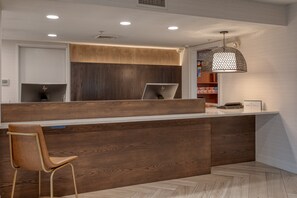 Un comptoir d’accueil avec un revêtement en bois, un ordinateur portable posé dessus et une suspension lumineuse au-dessus.