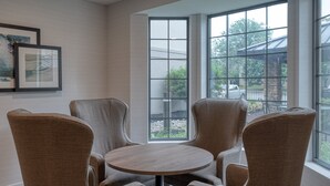 Una habitación con una mesa redonda y cuatro sillas, ventanas amplias con vistas al exterior y cuadros enmarcados en la pared.