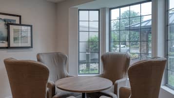 A room with a round table and four chairs, large windows with a view of the outdoors, and framed artwork on the wall.