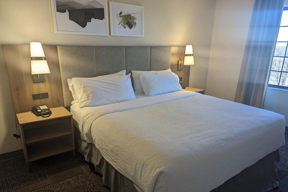Ein Hotelzimmer mit einem großen Bett, zwei Nachttischen mit Lampen, einem Telefon und einem Kunstwerk an der Wand.