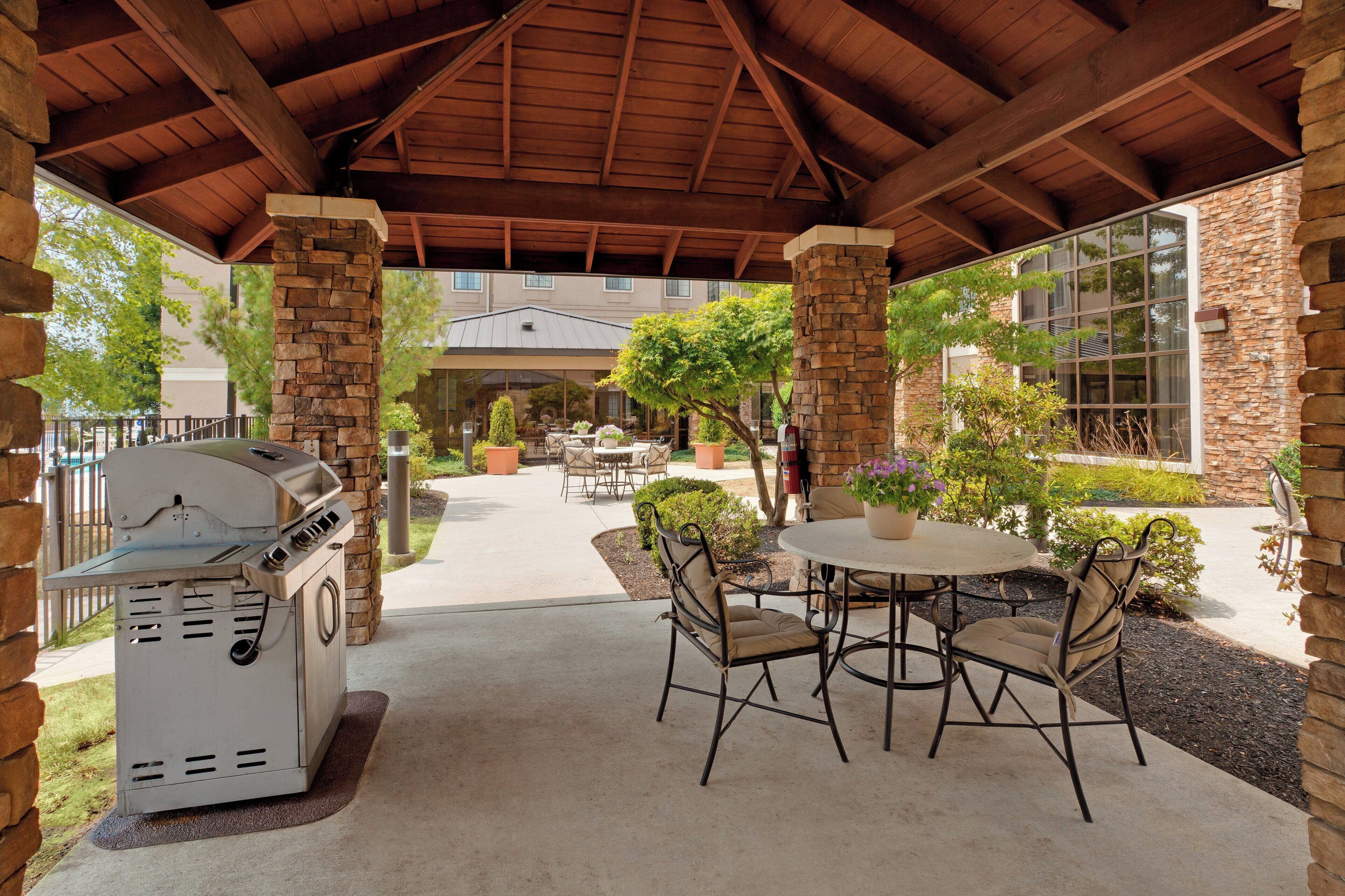 An outdoor patio with a grill, stone pillars, and a covered seating area with chairs and tables.