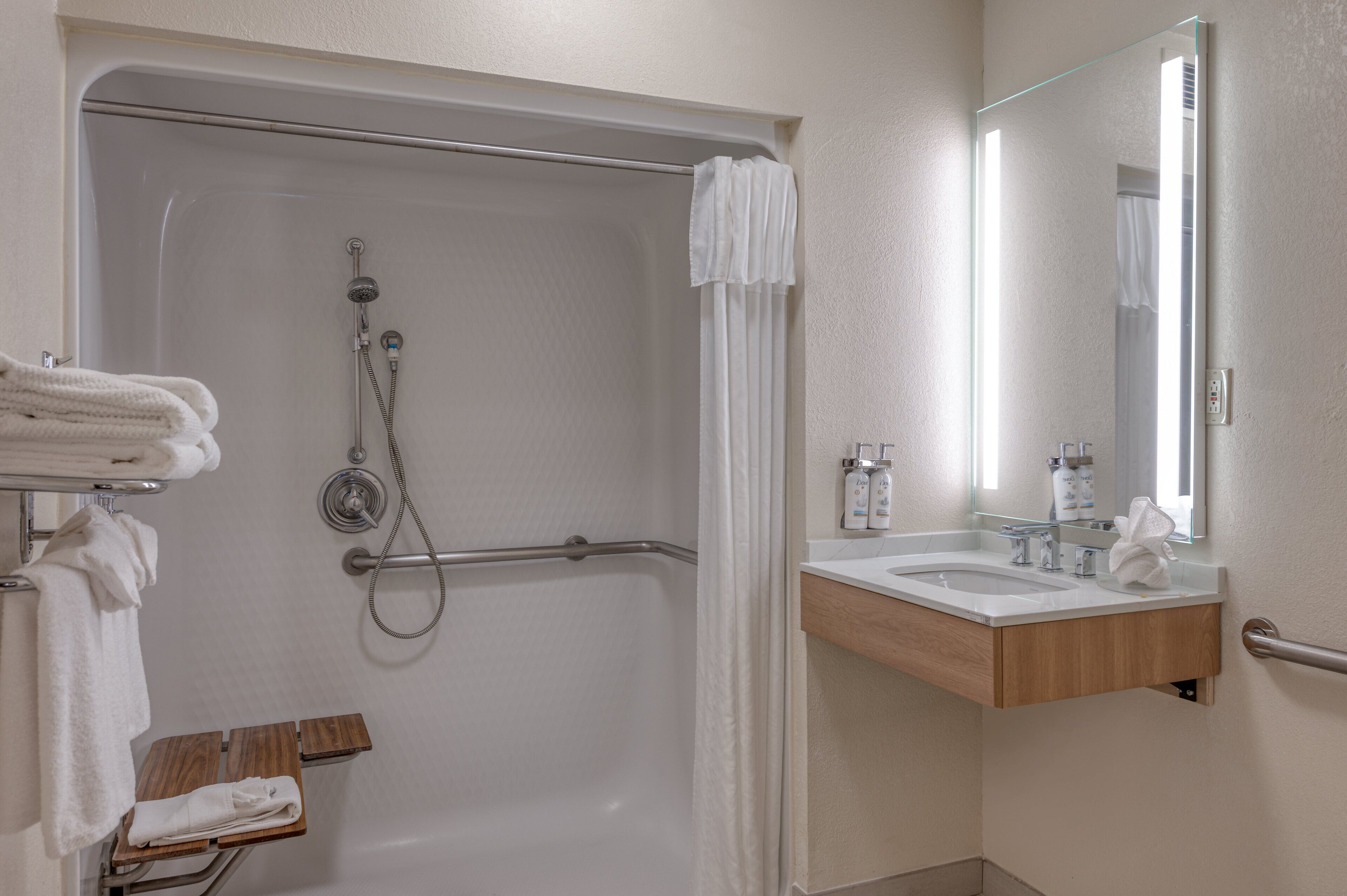 Un baño moderno con cabina de ducha, barras de apoyo, tocador con espejo y un perchero para toallas.
