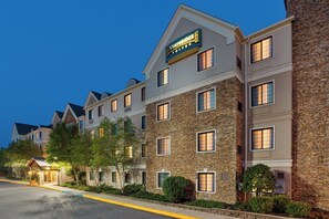 Un hôtel Staybridge Suites doté d’une façade en pierre, de nombreuses fenêtres et d’une entrée bien éclairée.