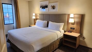 A hotel room with a large bed, two bedside tables, a nightstand, a window with curtains, and two wall-mounted lamps.