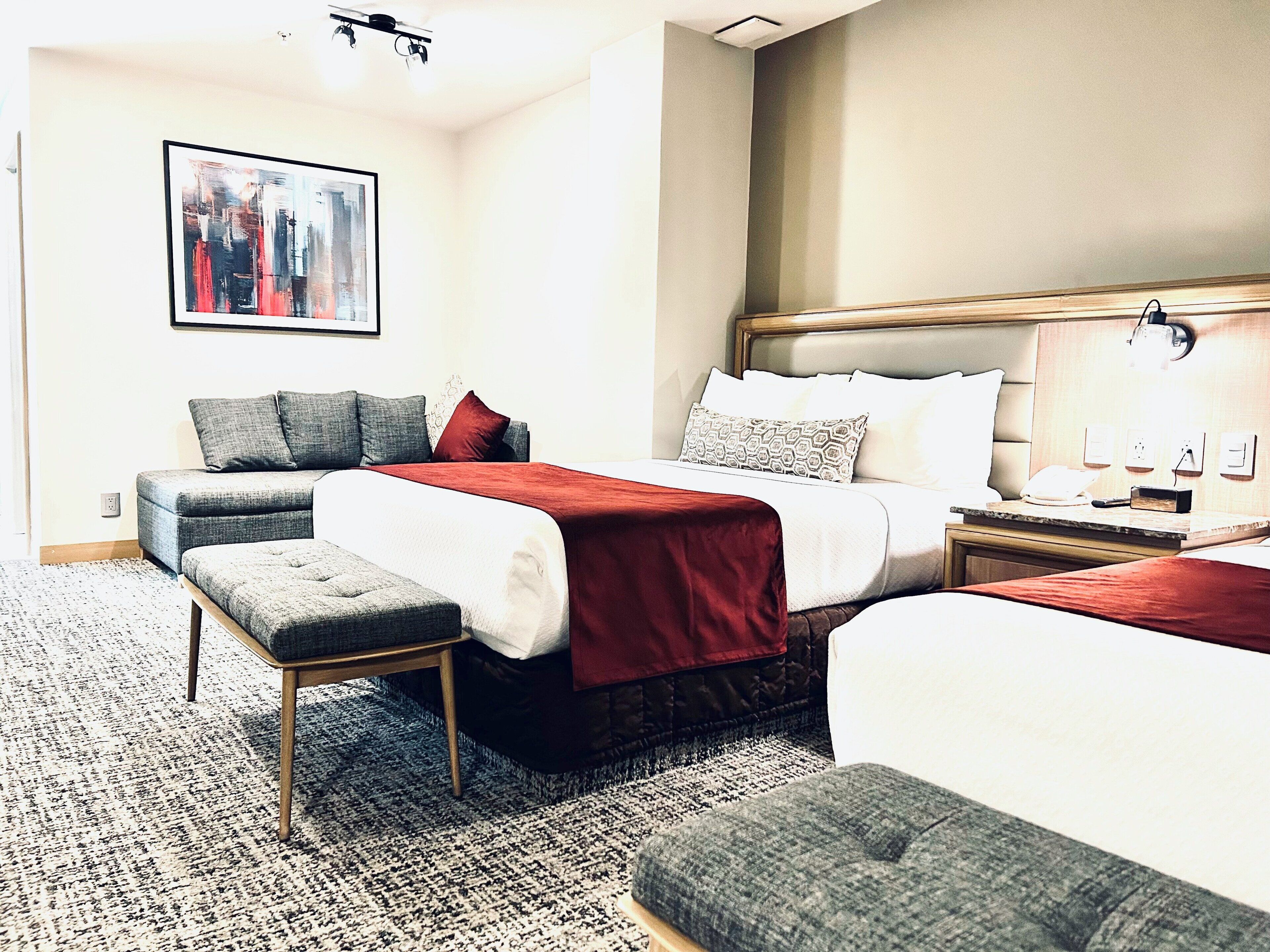 Een hotelkamer met een groot bed, een kleinere bank, een zitbankje en een nachtkastje met een lamp.