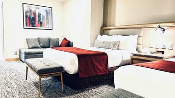 Een hotelkamer met een groot bed, een kleinere bank, een zitbankje en een nachtkastje met een lamp.