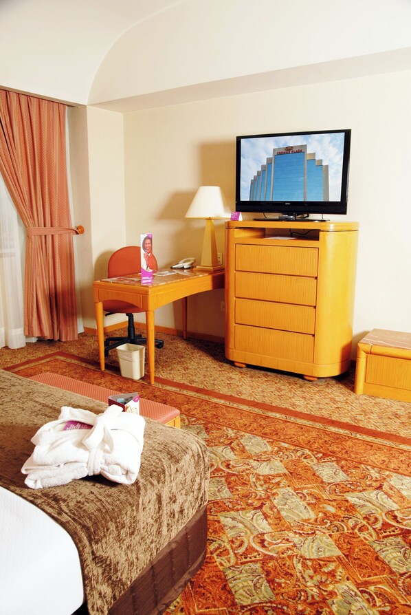 Habitación de hotel con cama, escritorio con lámpara, televisor y una mesita con teléfono.