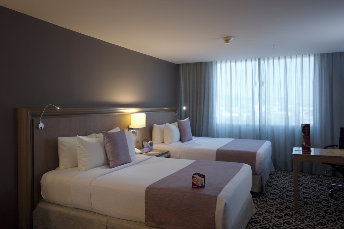 A hotel room with two beds, a desk, and a window with curtains.