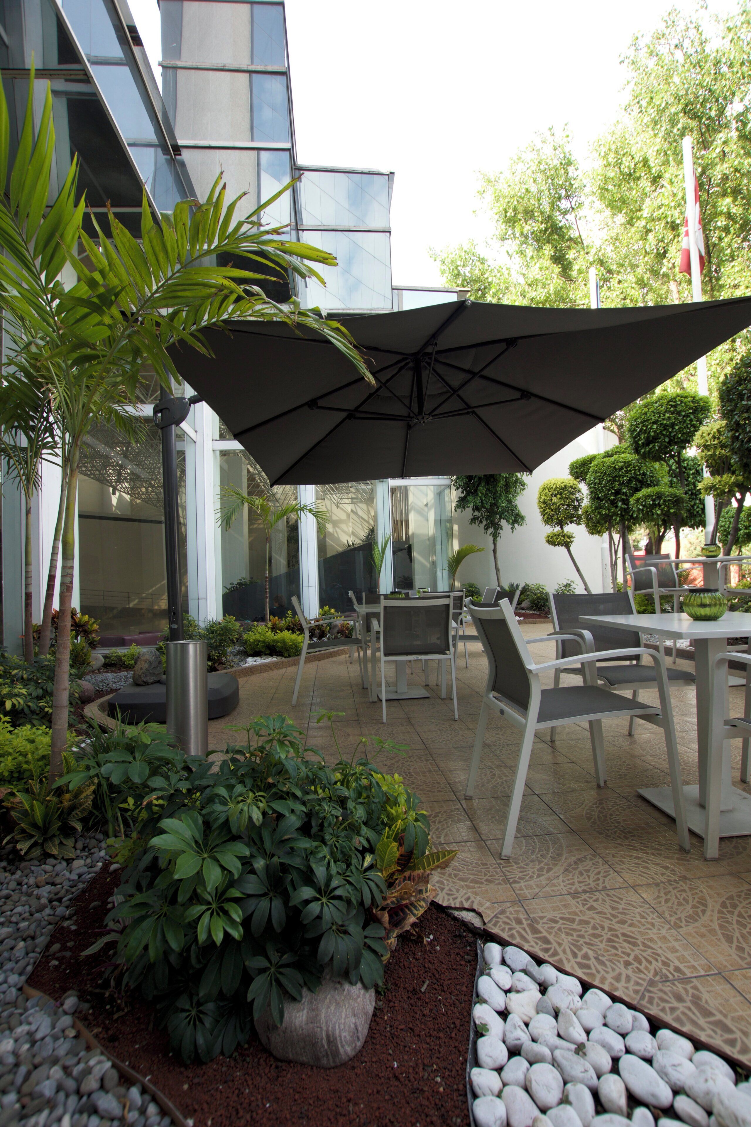 An outdoor patio area with a table and chairs, surrounded by potted plants and a large umbrella.