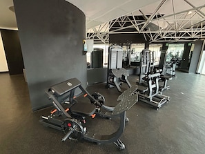 Un gimnasio con equipo de cardio, máquinas de pesas y un espejo grande.