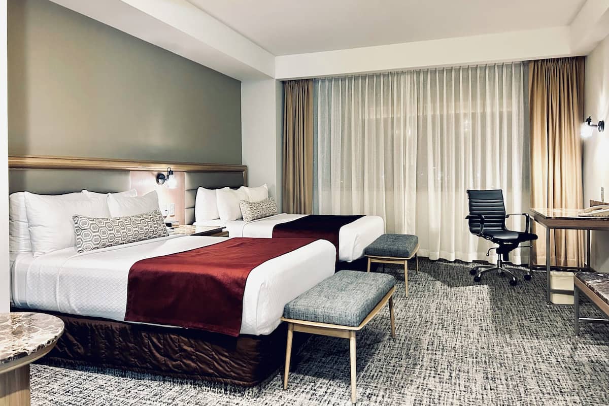 Habitación de hotel con dos camas, un escritorio, una silla y una mesita.