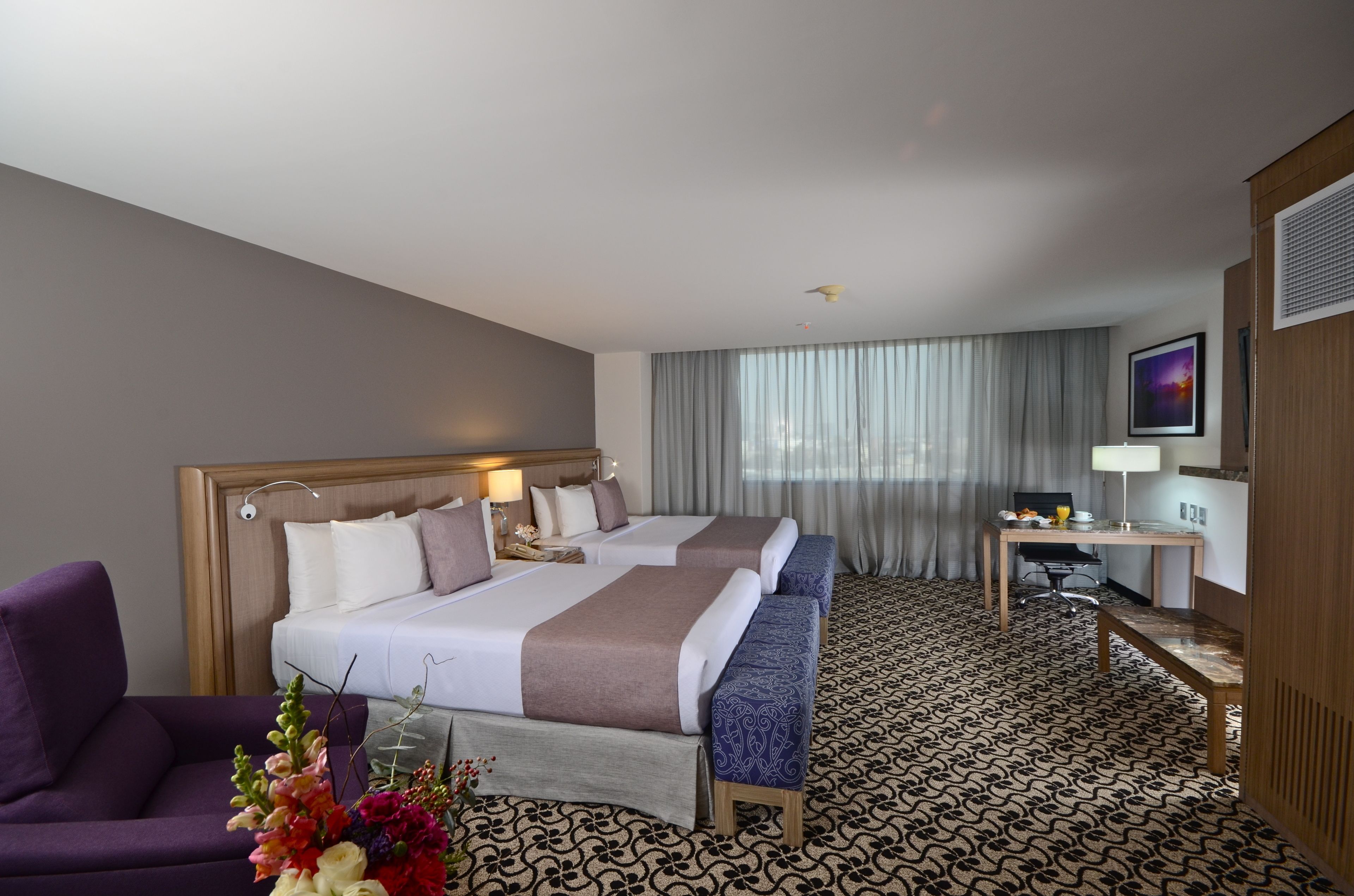 A hotel room with two beds, a desk, a chair, and a large window with curtains.