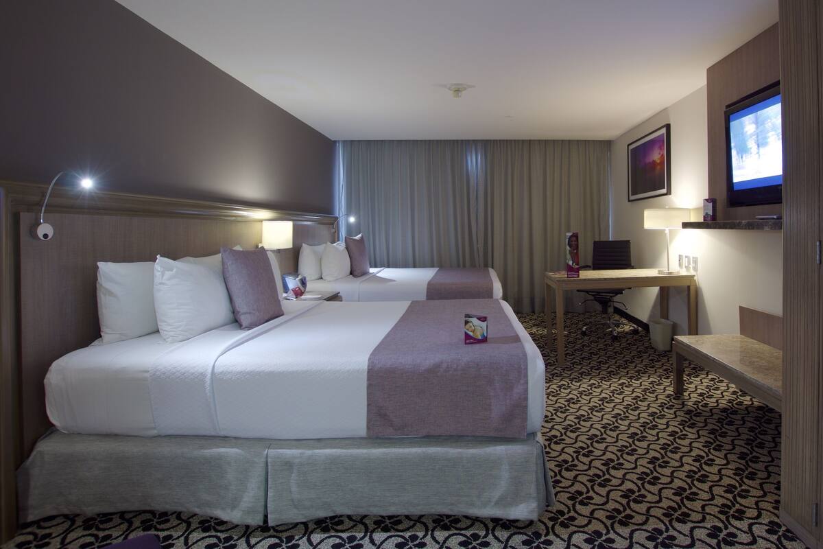 Una habitación de hotel con dos camas, un escritorio, un televisor y una alfombra estampada.