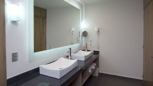 A modern bathroom with two sinks, a large mirror, and a hairdryer on the wall.