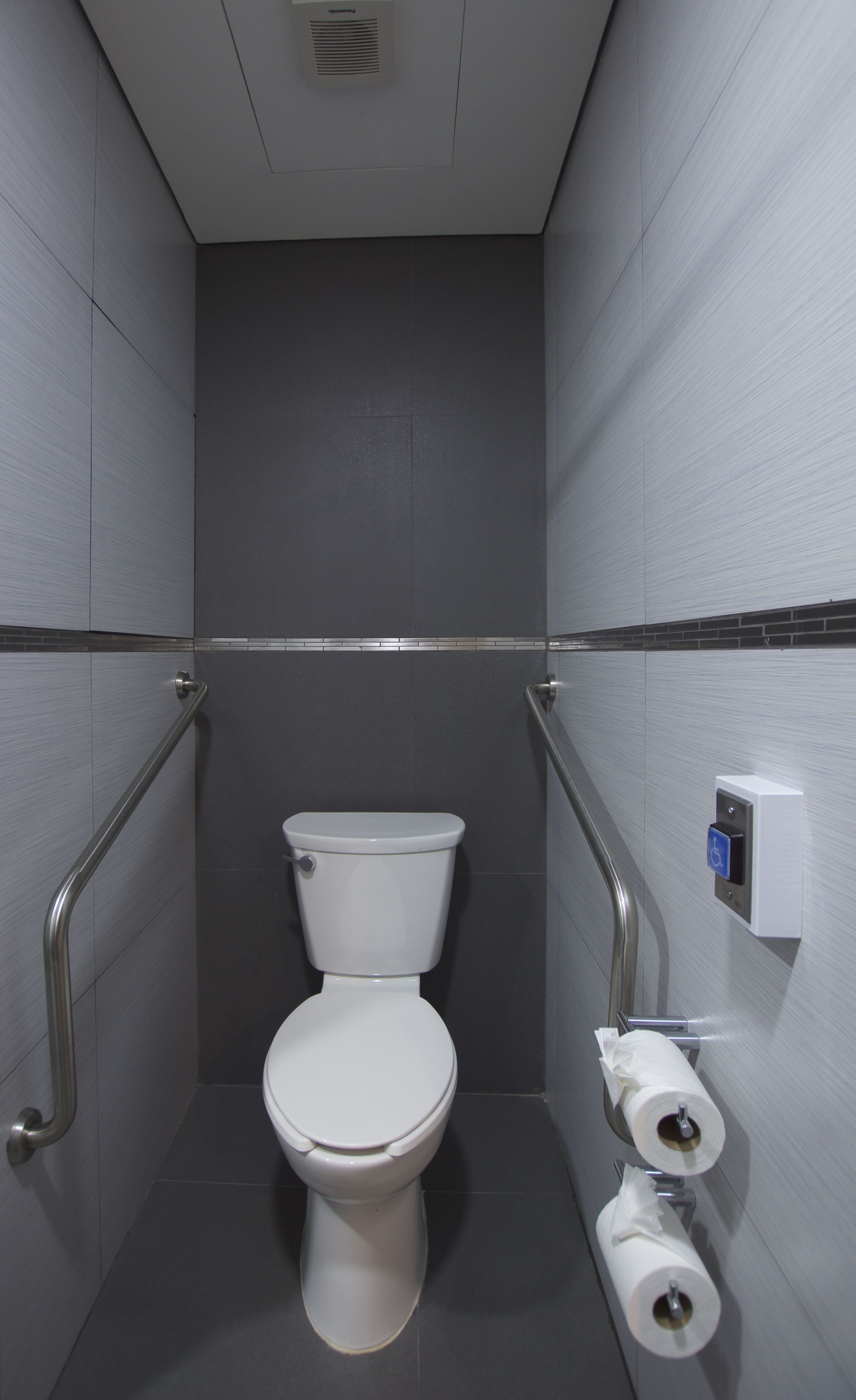 Une petite salle de bain moderne avec des toilettes blanches, un sèche-mains et un distributeur de serviettes en papier.
