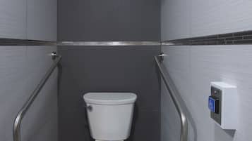 Une petite salle de bain moderne avec des toilettes blanches, un sèche-mains et un distributeur de serviettes en papier.